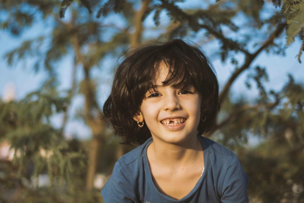 young brunette girl missing front tooth smiling outside