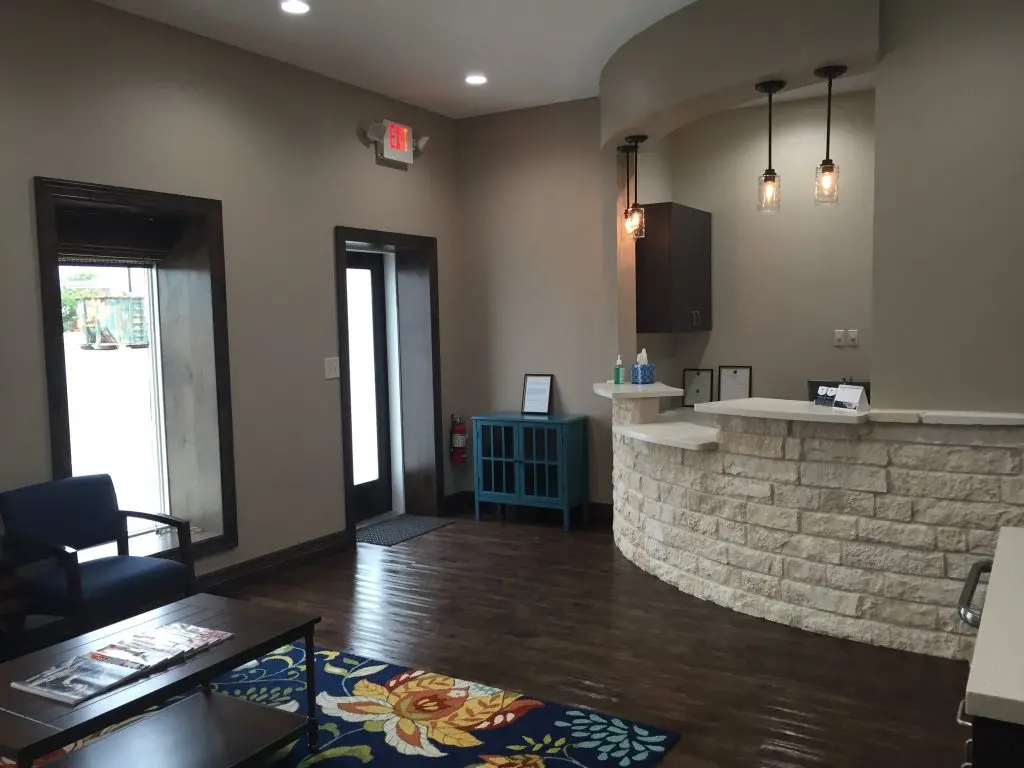 Bright and inviting dental office reception area featuring a curved stone desk, cozy seating, and natural light—reflecting a warm, professional environment designed for patient comfort and care.