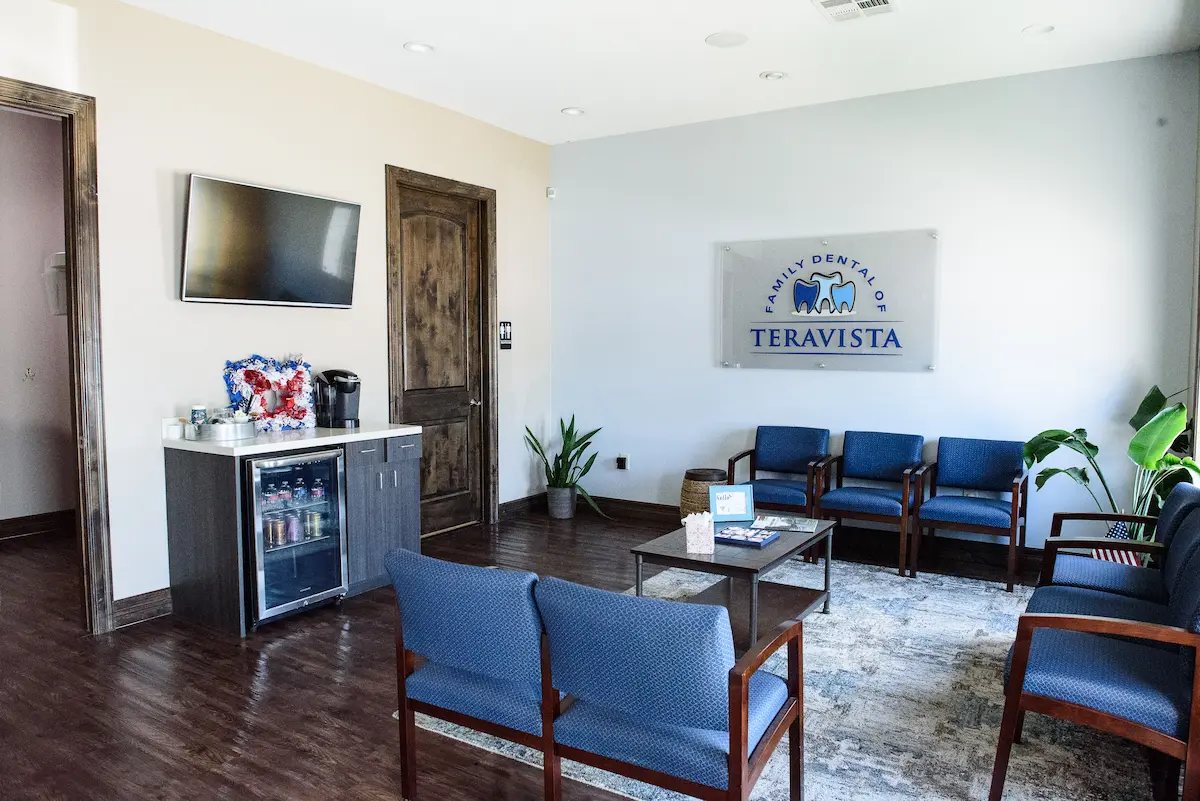 Comfortable dental office waiting room with blue cushioned chairs, refreshment station, and branded wall signage—creating a warm, professional space where patients feel relaxed before their appointments.